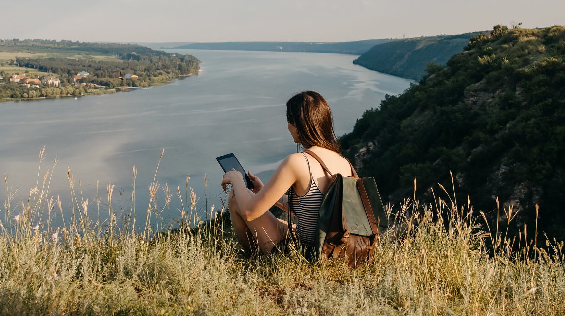 Młoda kobieta z tabletem odpoczywa na wzgórzu z widokiem na rzekę